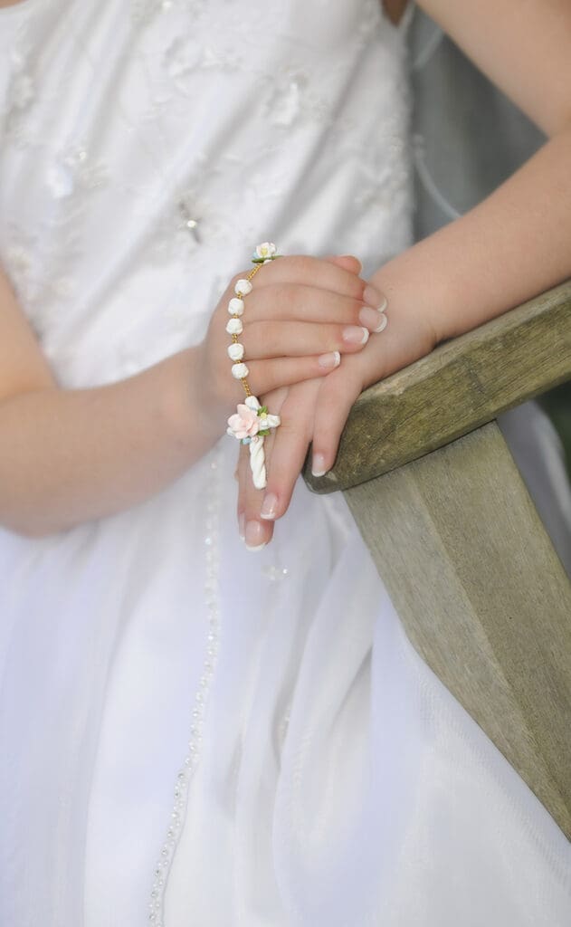 A woman in white holding a rosary and wearing wedding rings.