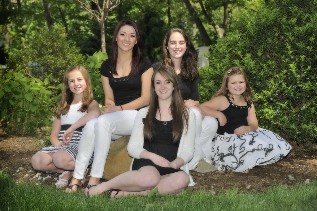 A group of girls sitting on the ground in front of trees.