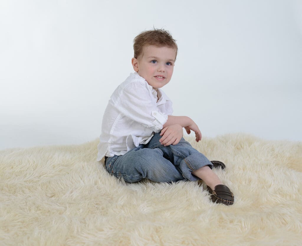 A young boy sitting on the floor in front of a white wall.