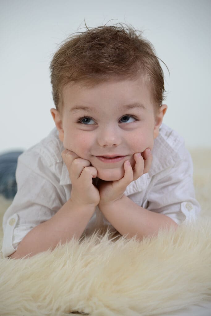 A baby laying on the ground with his hands under its chin.