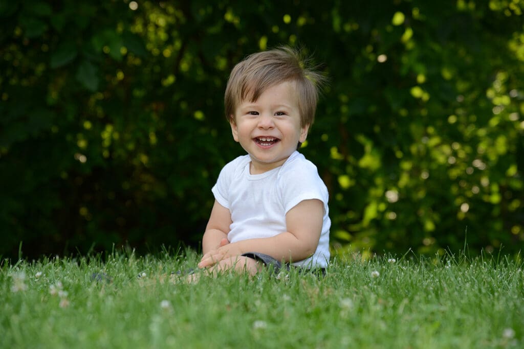 A baby sitting in the grass smiling for the camera.