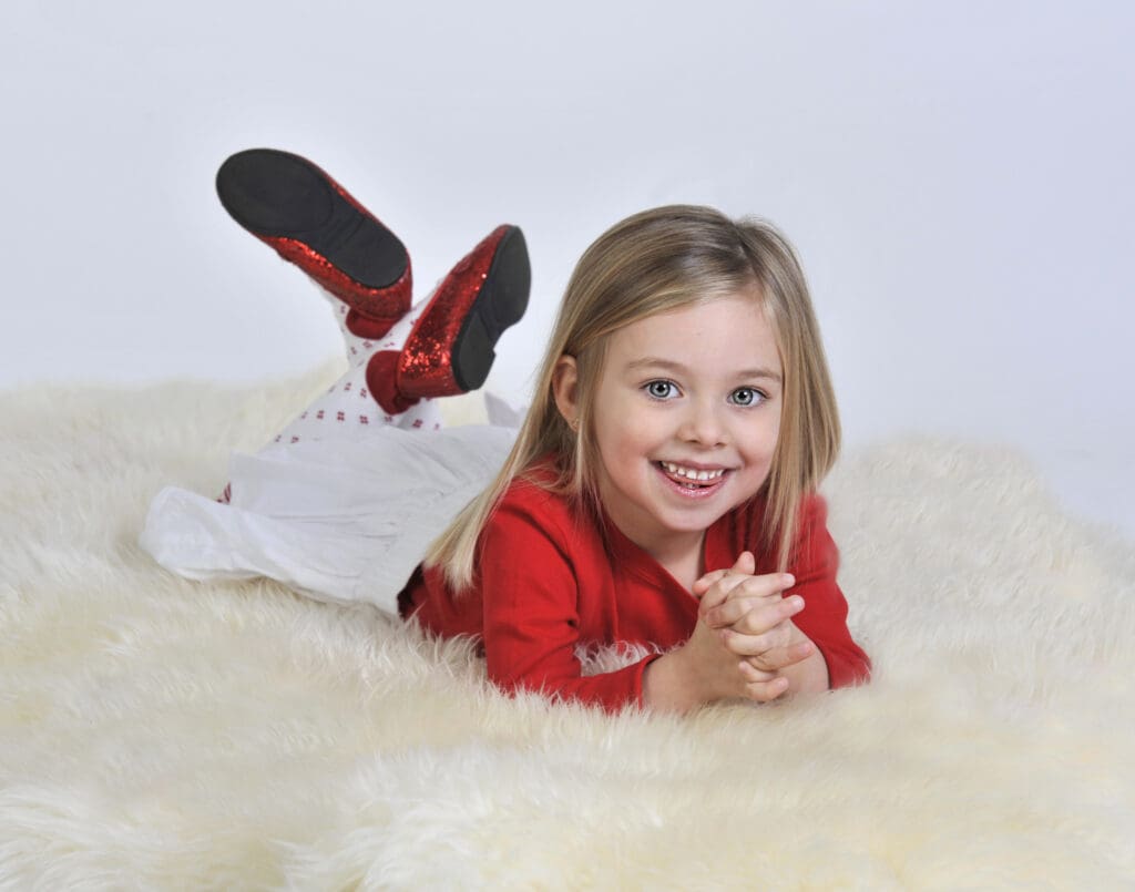 A little girl laying on the floor in front of a white wall.