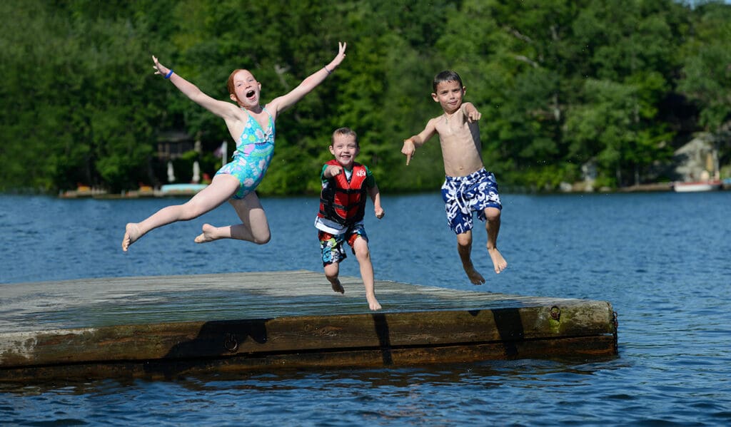 Three children jumping off a dock into the water.