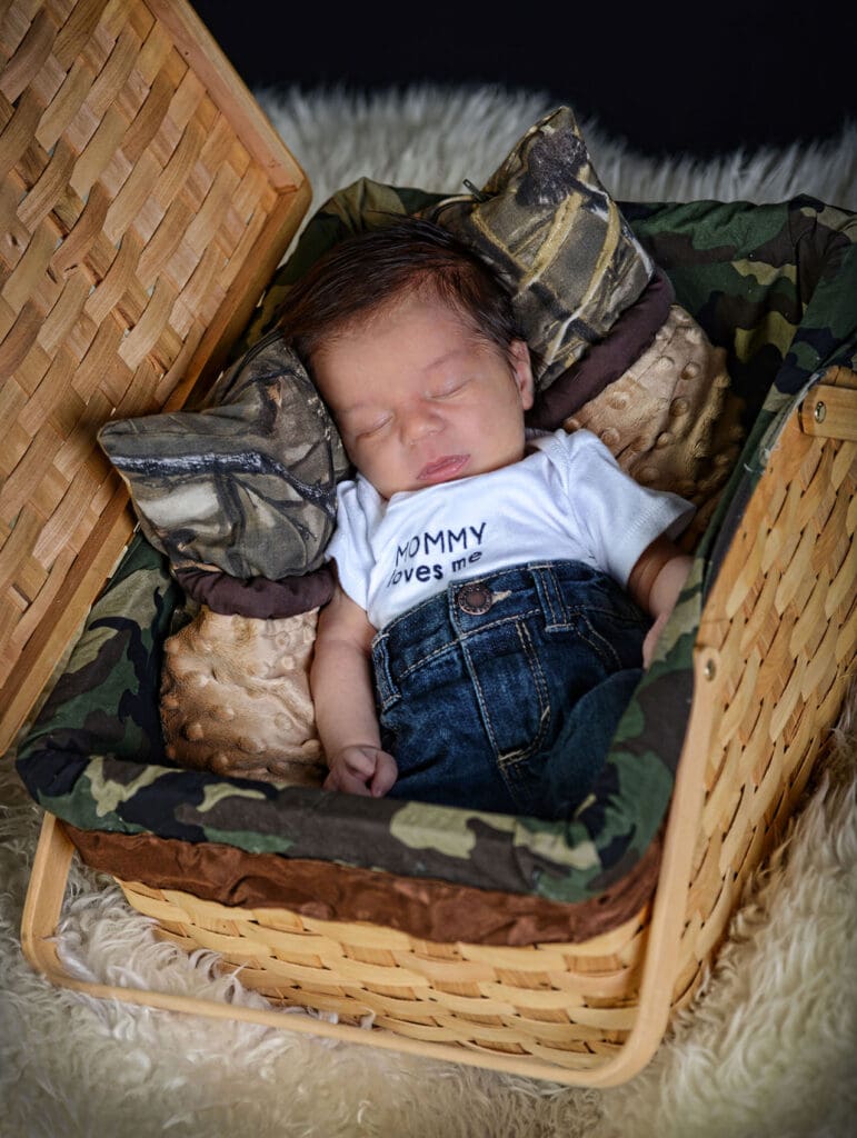 A baby is sleeping in a basket with camouflage material.