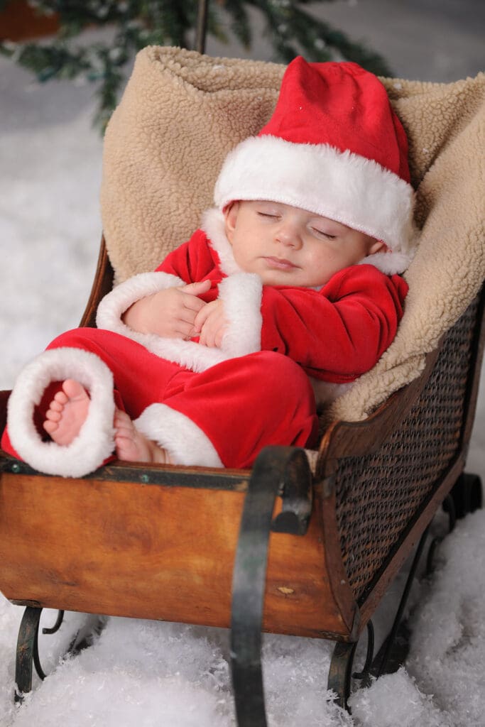 A baby in santa suit sleeping on top of a suitcase.