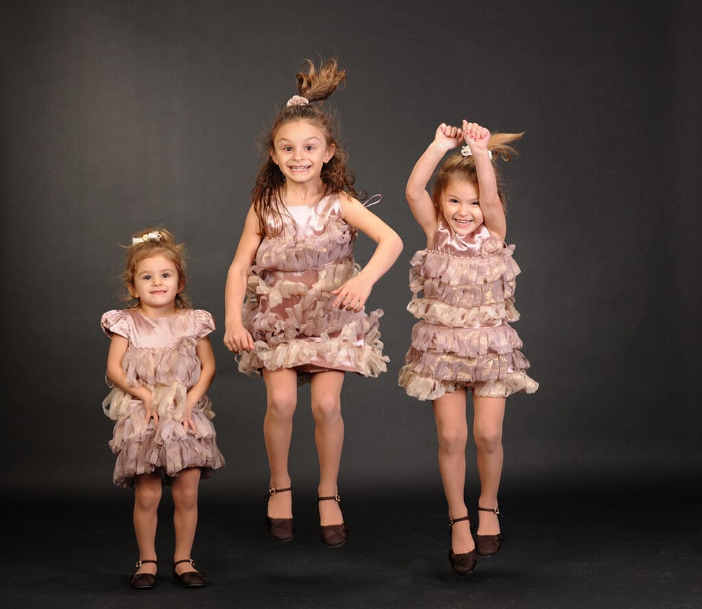 Three little girls in dresses posing for a picture.