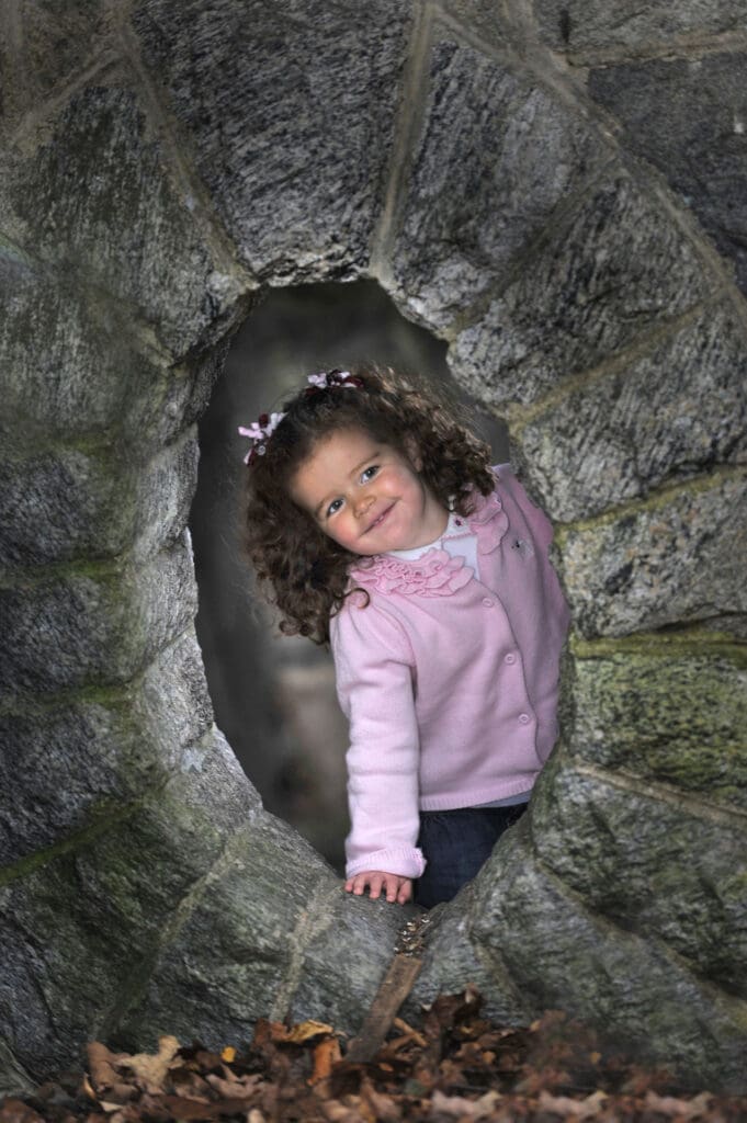 A little girl is smiling in the hole of an outdoor play structure.