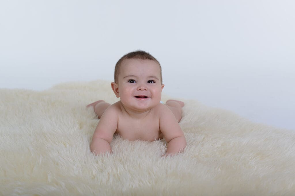 A baby is smiling while laying on the floor.