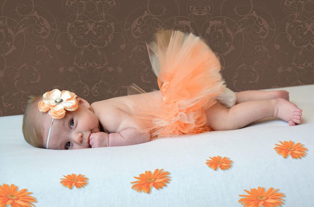 A baby girl in an orange tutu and flower headband.