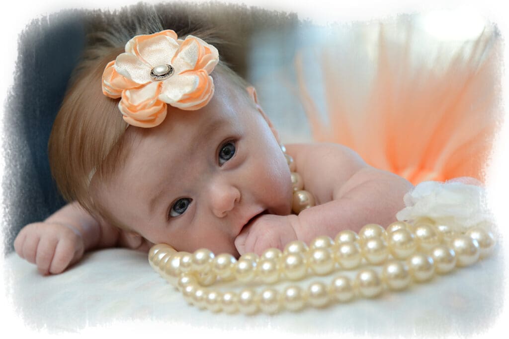 A baby girl with pearls and a flower in her hair.