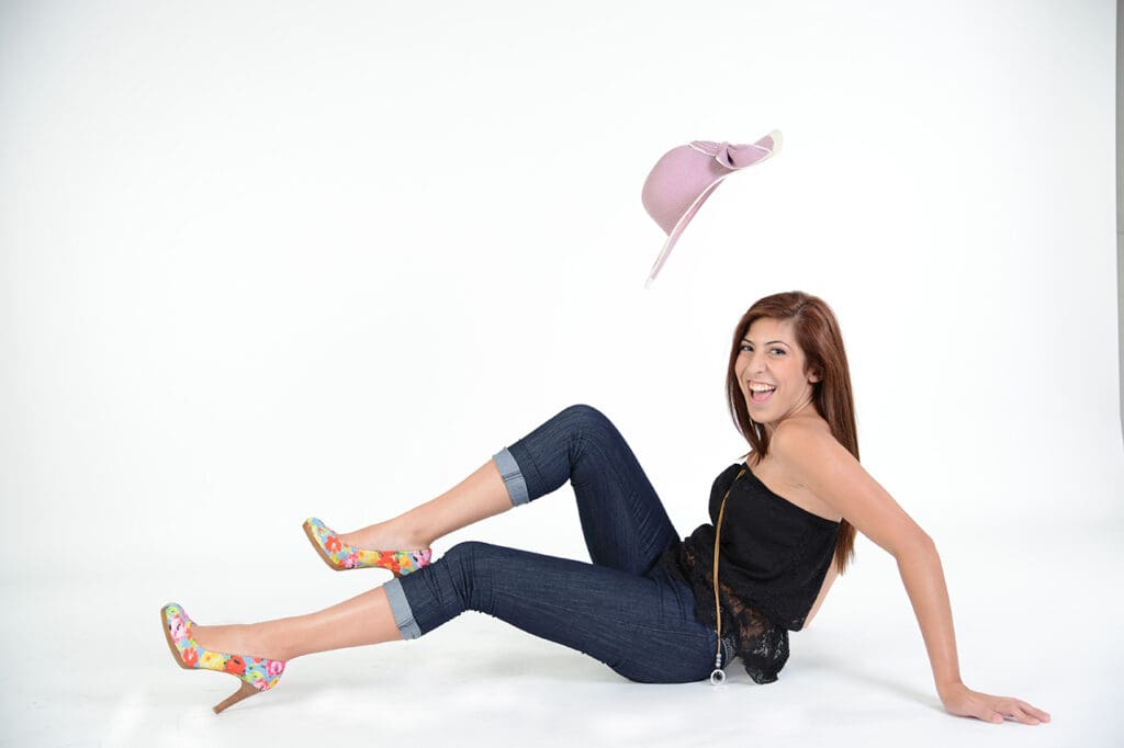 A woman in black shirt and blue jeans sitting on ground.