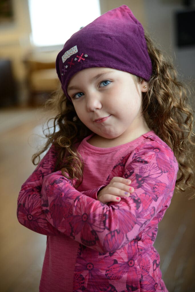 A little girl with her arms crossed wearing a headband.