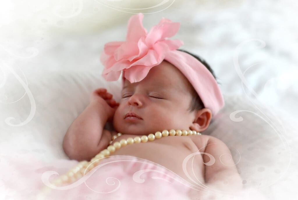 A baby girl wearing a pink bow and pearls.