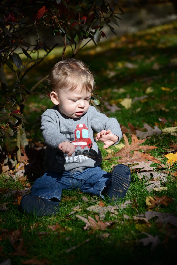 A little boy sitting on the ground in the grass.