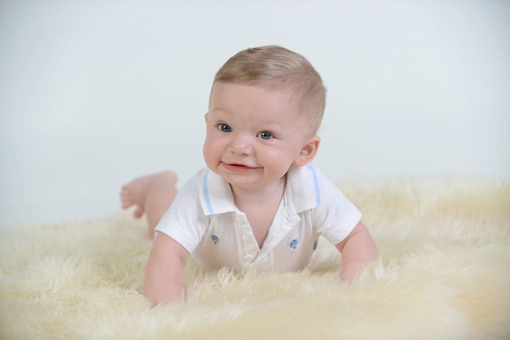 A baby is smiling while laying on the floor.