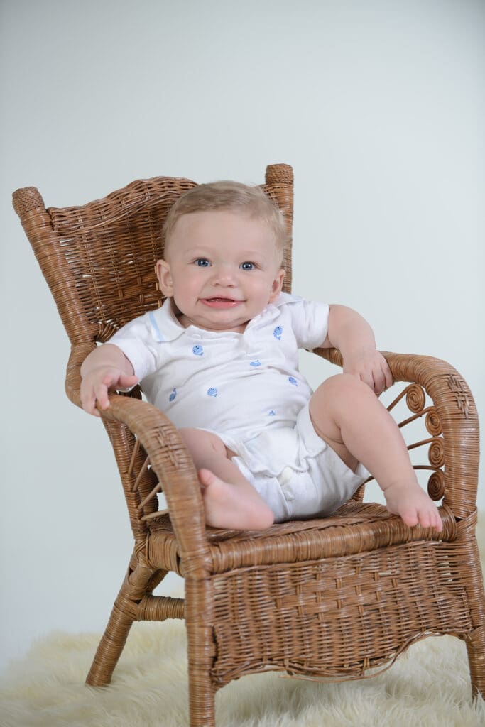 A baby sitting in a wicker chair wearing diapers.