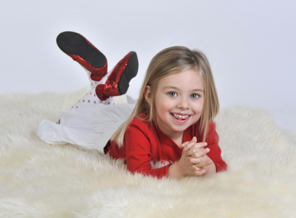 A little girl laying on the floor in front of a white wall.