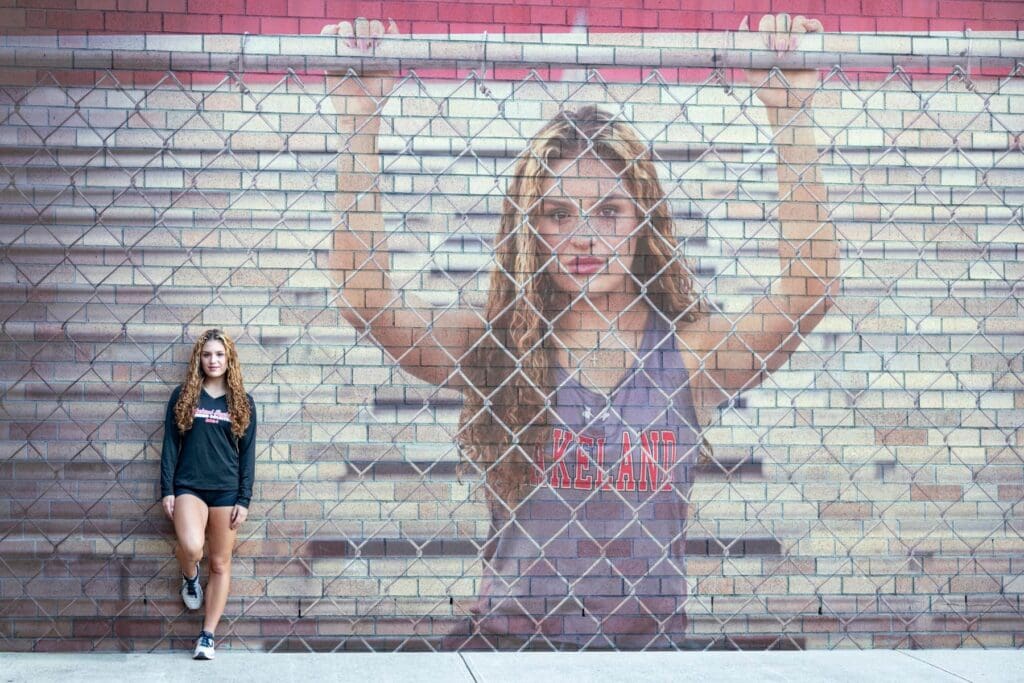 A woman standing next to a brick wall with a picture of a girl on it.