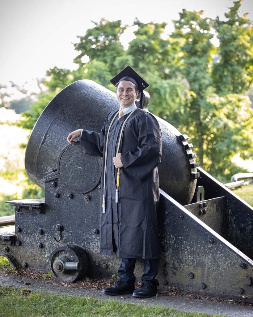 A man in cap and gown standing next to an old train.