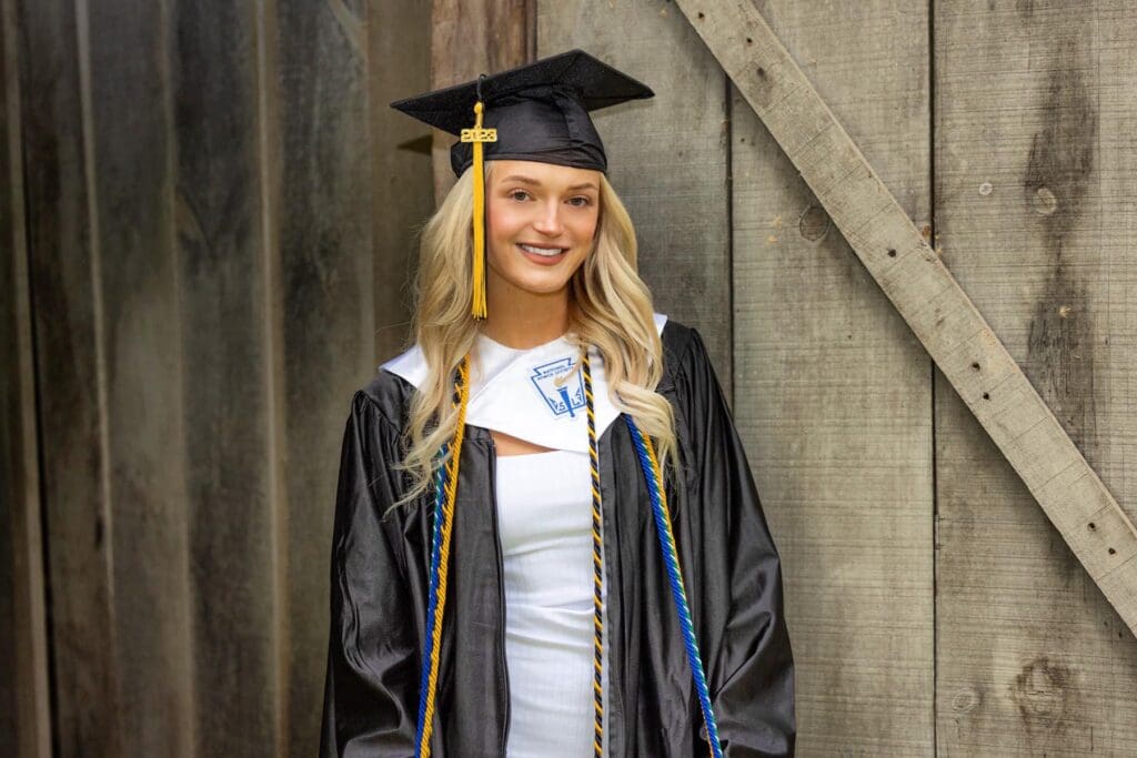 A girl in graduation attire standing next to a wooden wall.