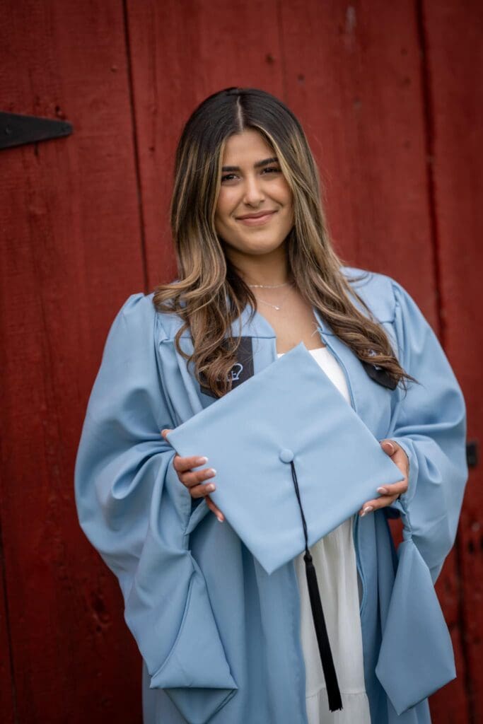 A woman in blue graduation gown holding her cap.